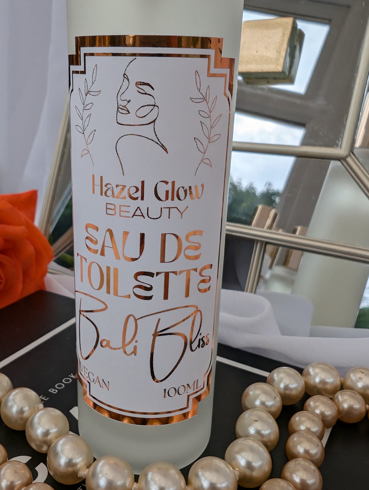 Bottle of Hazel Glow Beauty Eau de Toilette Bali Bliss with decorative pearls and a mirror in the background.