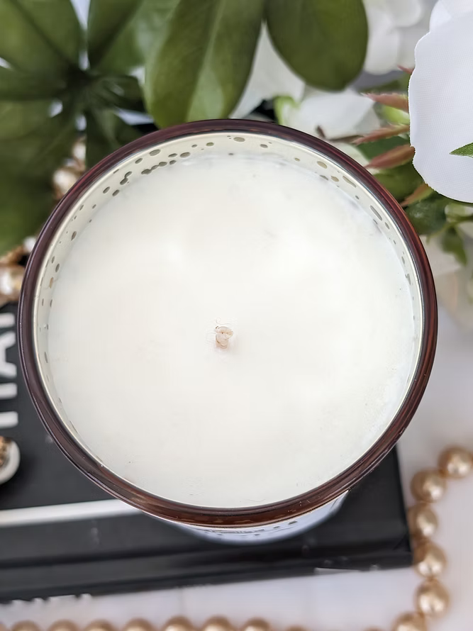 Top view of a white candle in a glass holder with decorative elements in the background