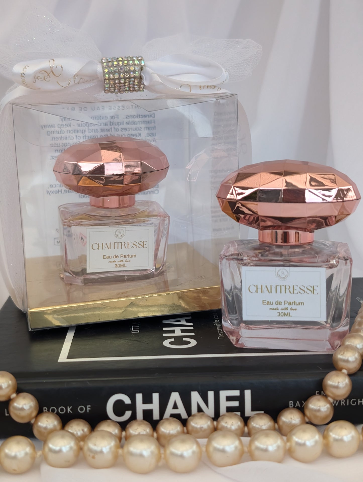 Two Chantresse perfume bottles with rose gold caps on a Chanel book, surrounded by pearls.