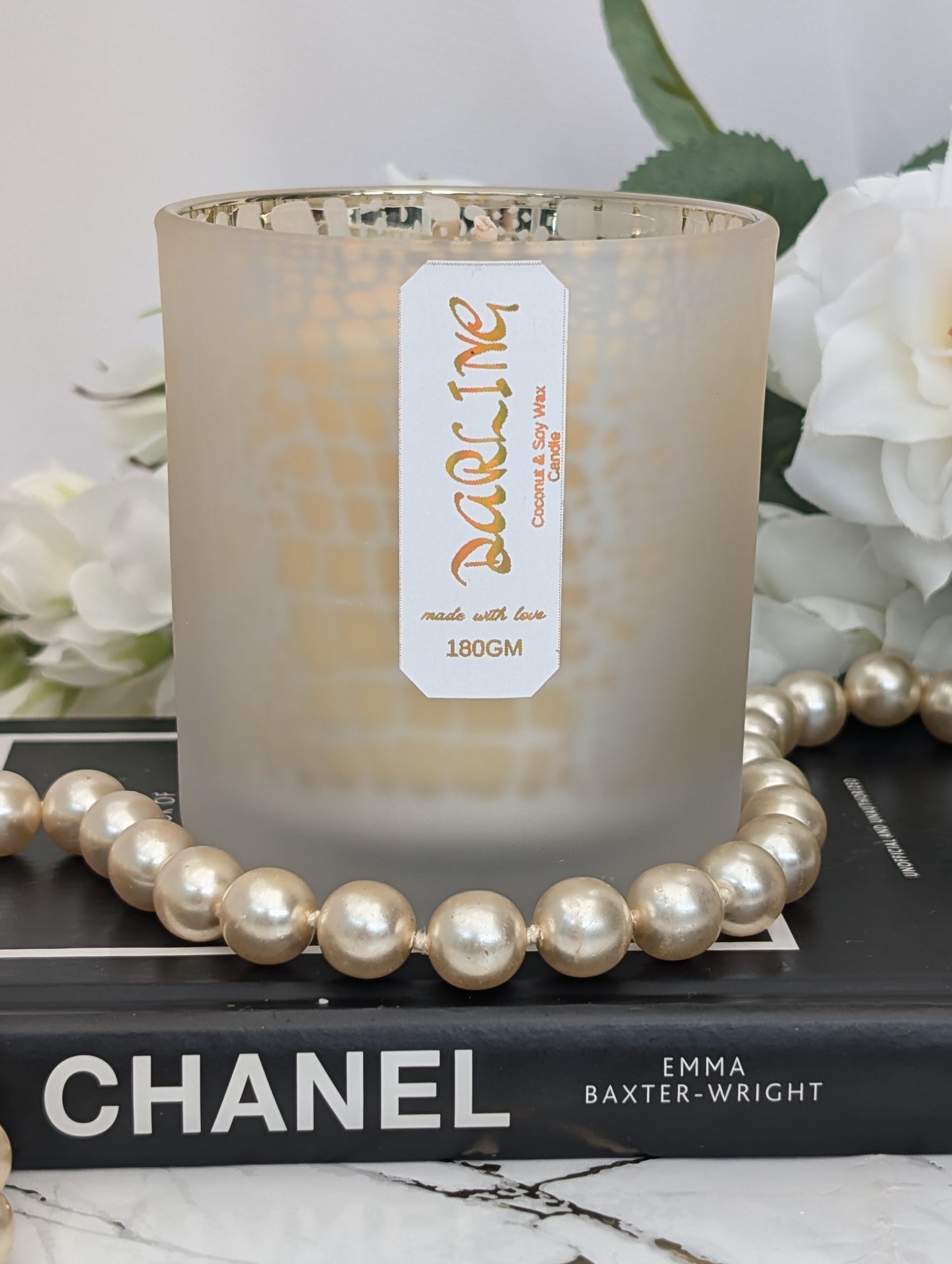 Candle with a label on a Chanel book surrounded by pearls and flowers