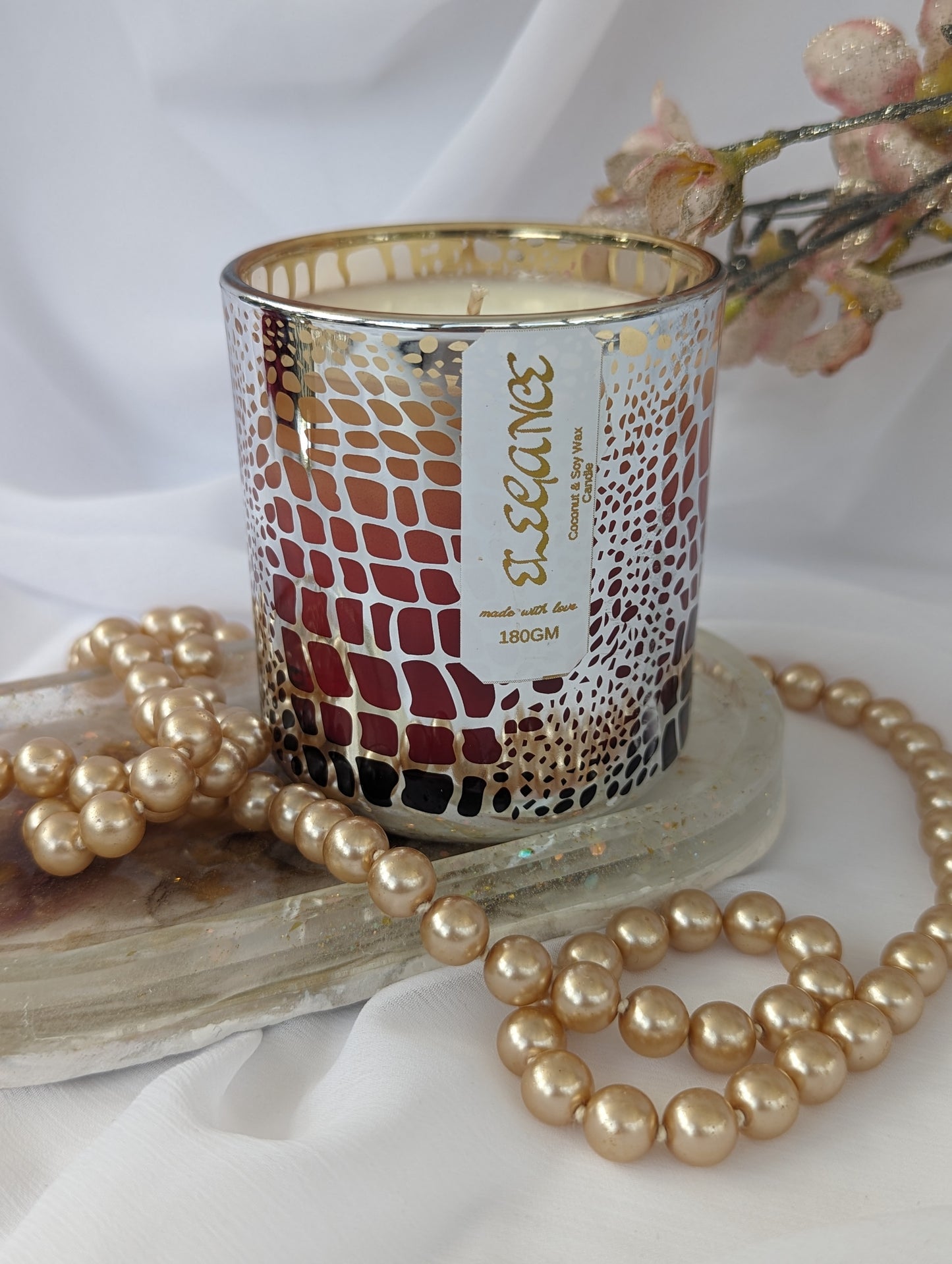 Decorative candle with a patterned design on a white surface with pearls and flowers.