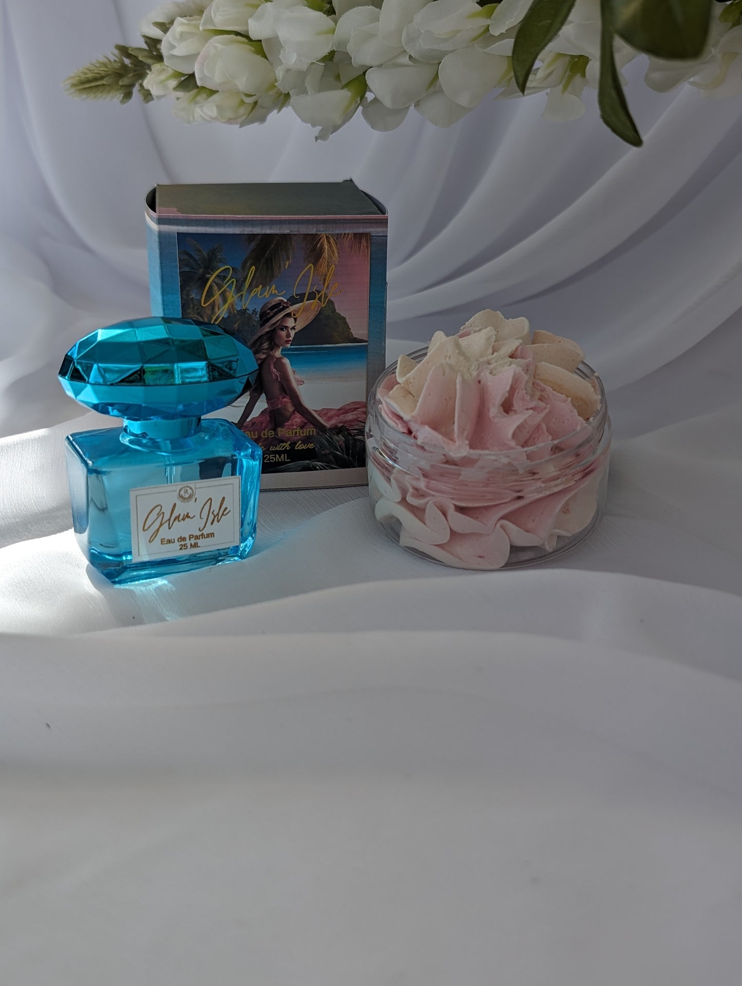 Blue perfume bottle, pink flower arrangement, and scenic postcard on a white surface
