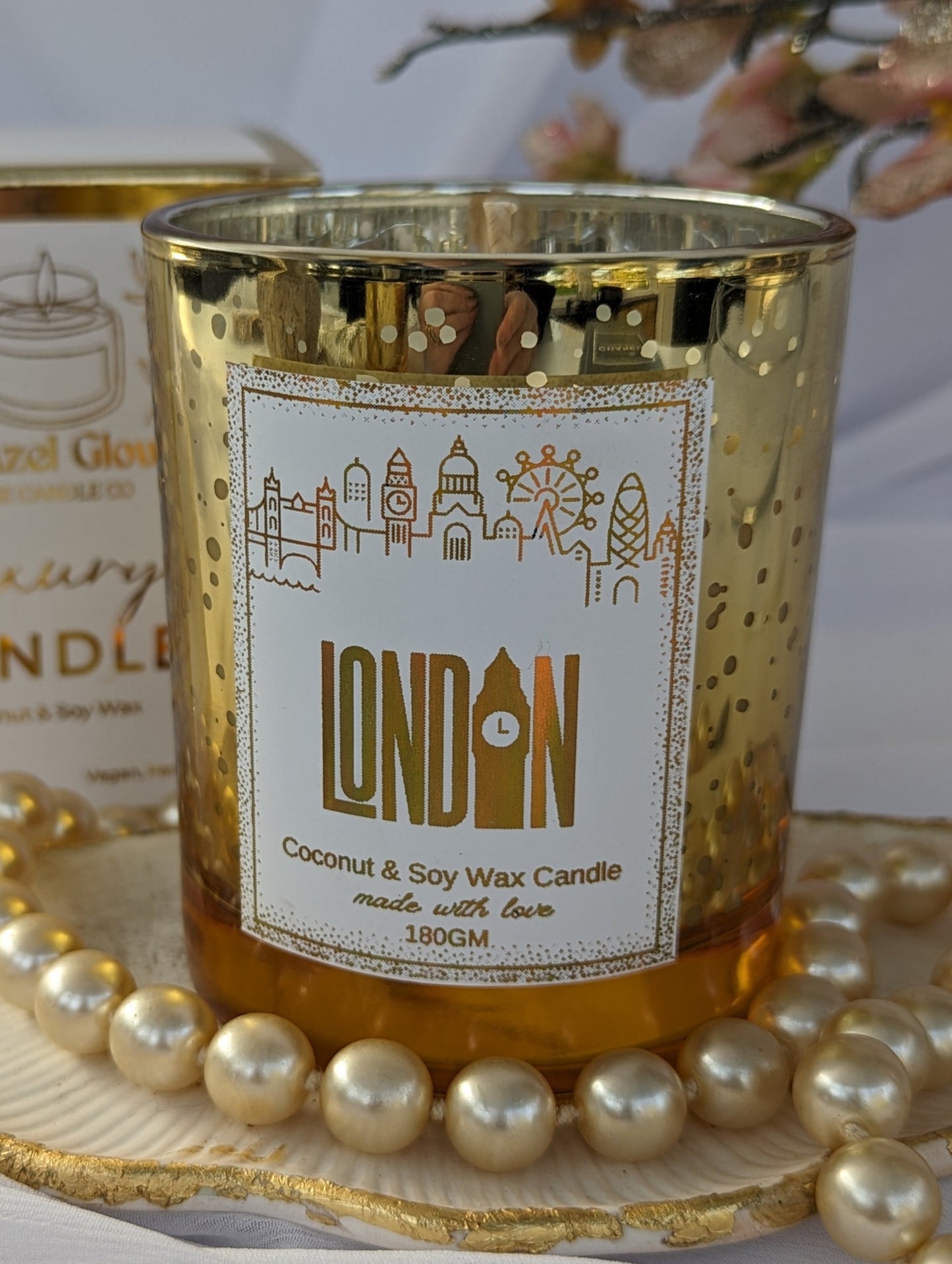 Gold candle with 'London' label on a decorative tray with pearls and flowers.