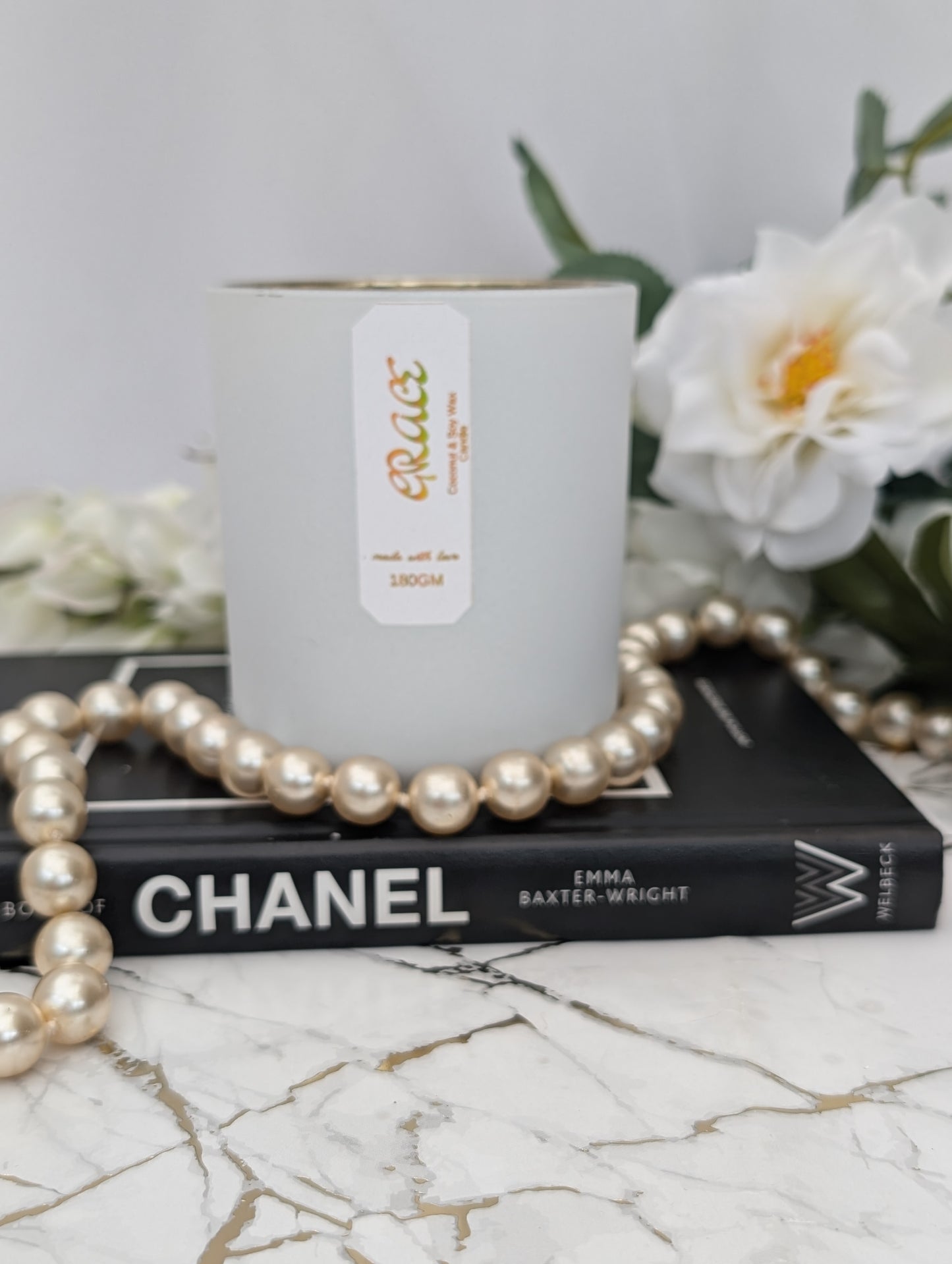 Luxury "Grace" candle on a Chanel book with flowers and pearls in the background