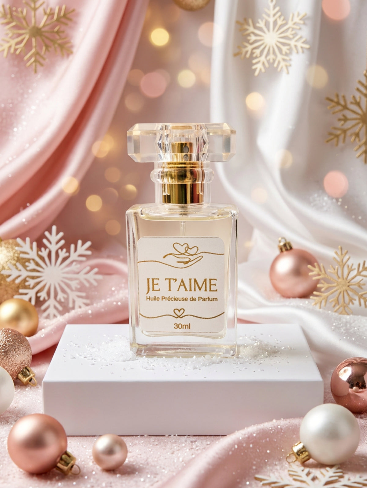 Luxury perfumed spray oil in Je T'Aime fragrance by Hazel Glow. Shown on a white plinth against a pastel pink background with pink Christmas baubles and white snowflakes