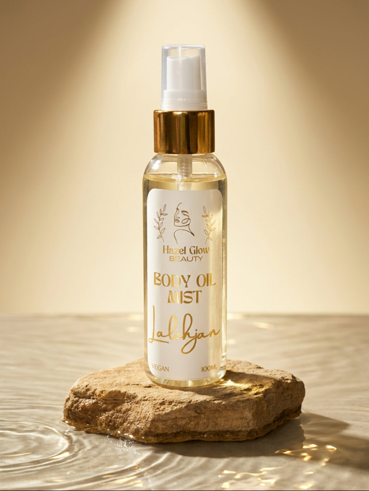 A clear spray bottle of Lalehjan Body Oil Mist by Hazel Glow with a white label and gold lettering, featuring a gold pump collar and white cap, set against a rough stone plinth in water