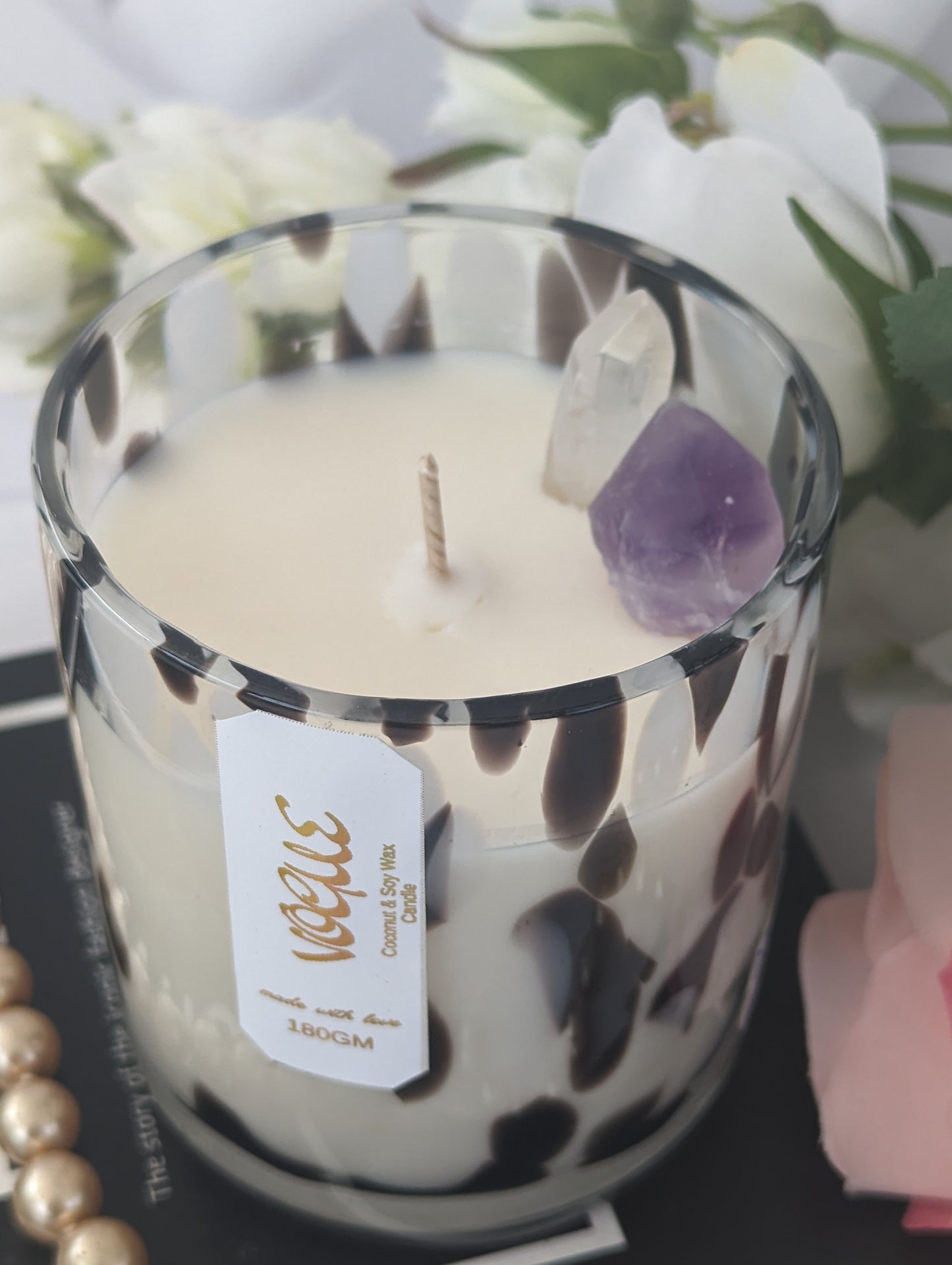 Vogue Luxury Candle showing candle top with decorative crystals and a Vogue label, surrounded by white flowers.