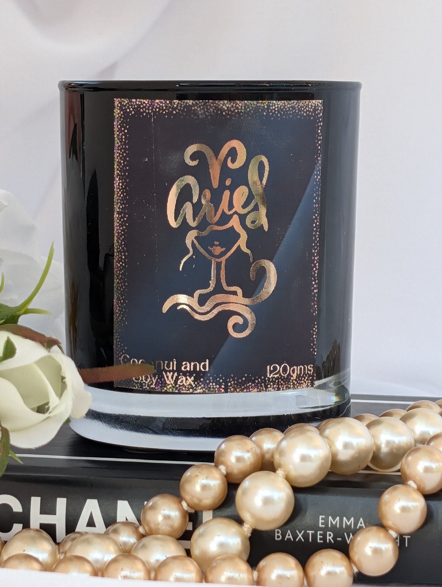 Aries gold and black  zodiac candle styled on a book with pearl beads in the foreground.