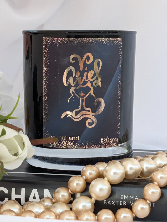 Aries gold and black  zodiac candle styled on a book with pearl beads in the foreground.