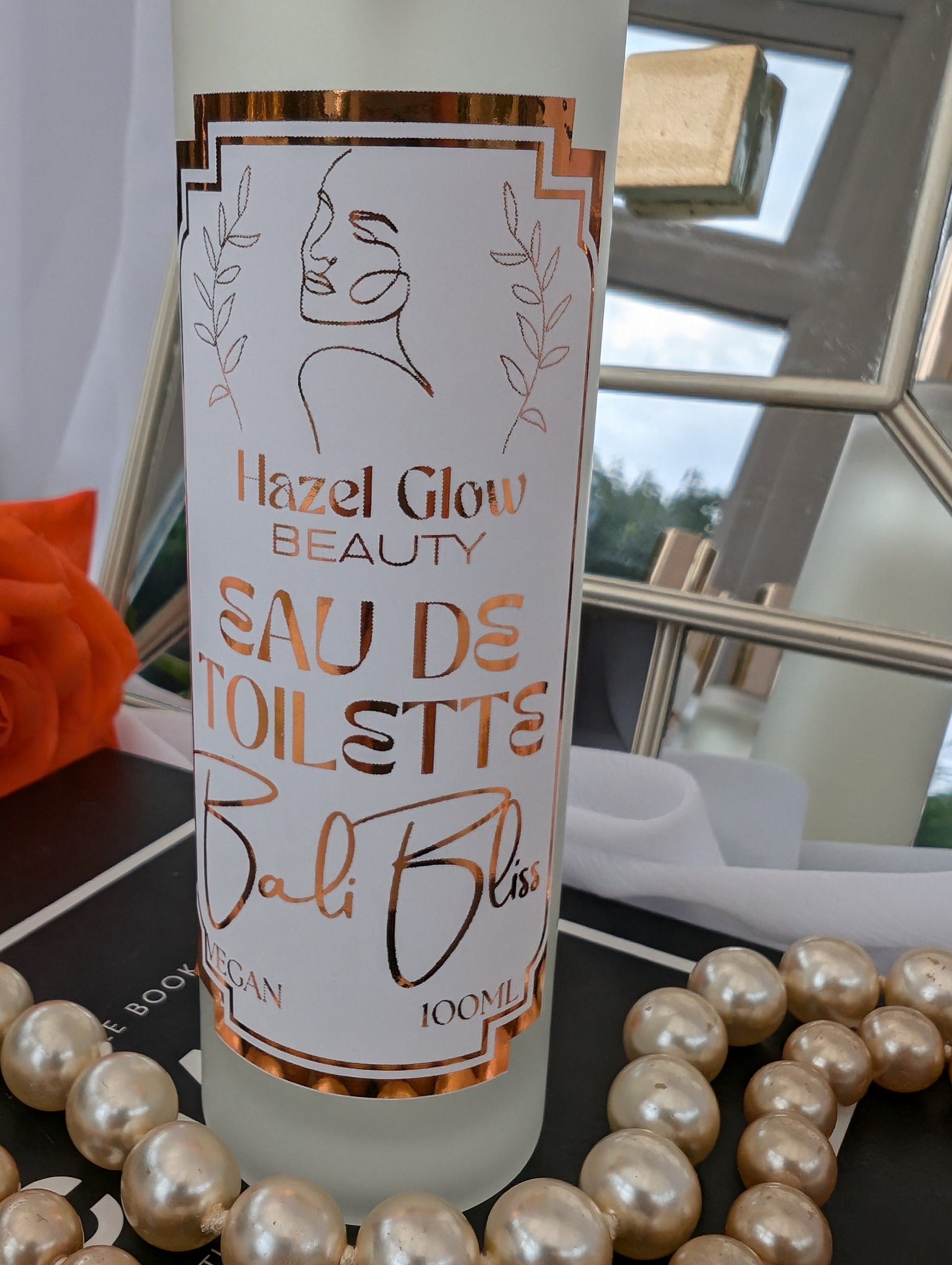 Bottle of Hazel Glow Beauty Eau de Toilette Bali Bliss with decorative pearls and a mirror in the background.