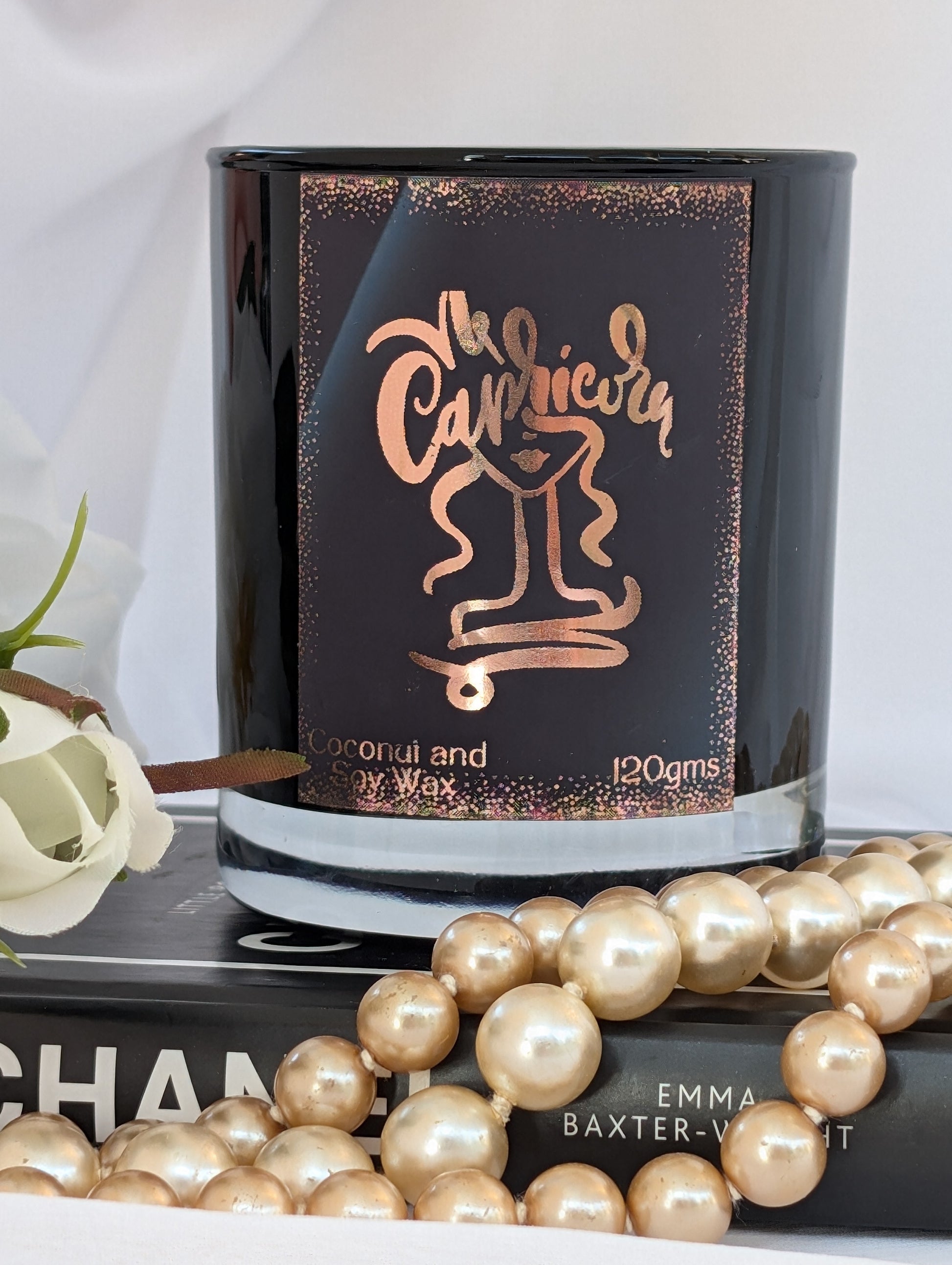 Candle with 'Capricorn' design on packaging, surrounded by pearls and a book