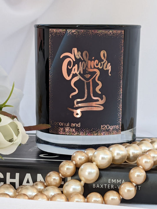 Candle with 'Capricorn' design on packaging, surrounded by pearls and a book