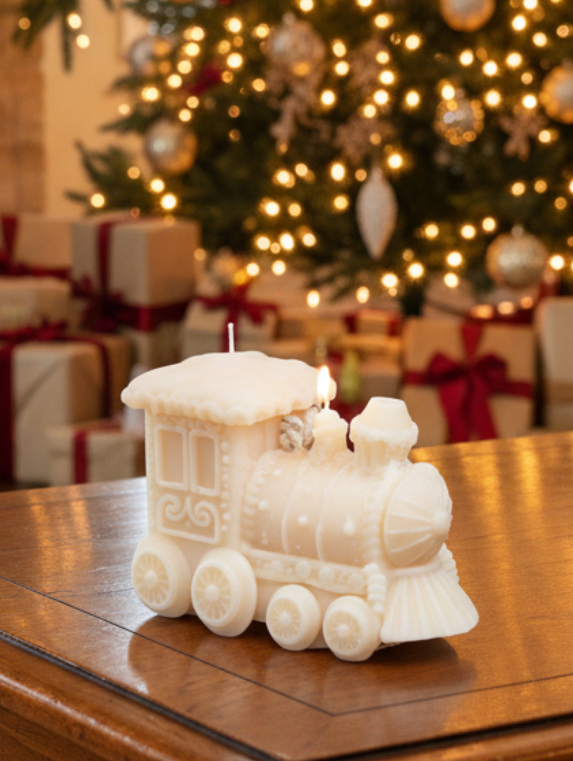 A cream-colored decorative train-shaped candle  on a wooden table with Christmas tree and presents in the background