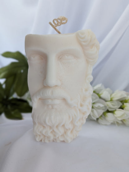 Candle shaped like a face with a beard on a white surface with greenery in the background