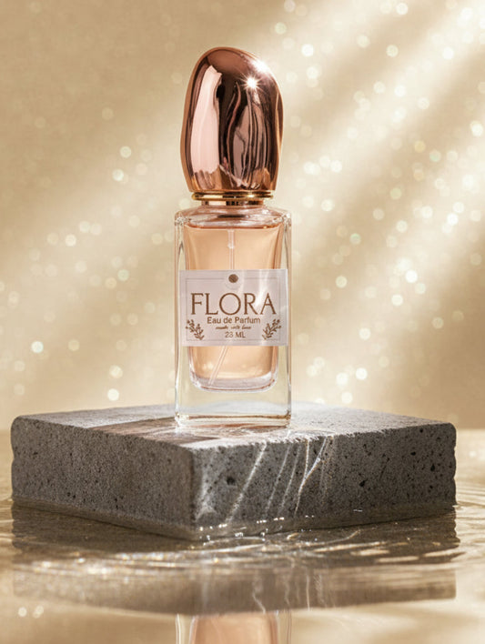Perfume bottle labeled 'Flora' on a reflective surface with a sparkling background
