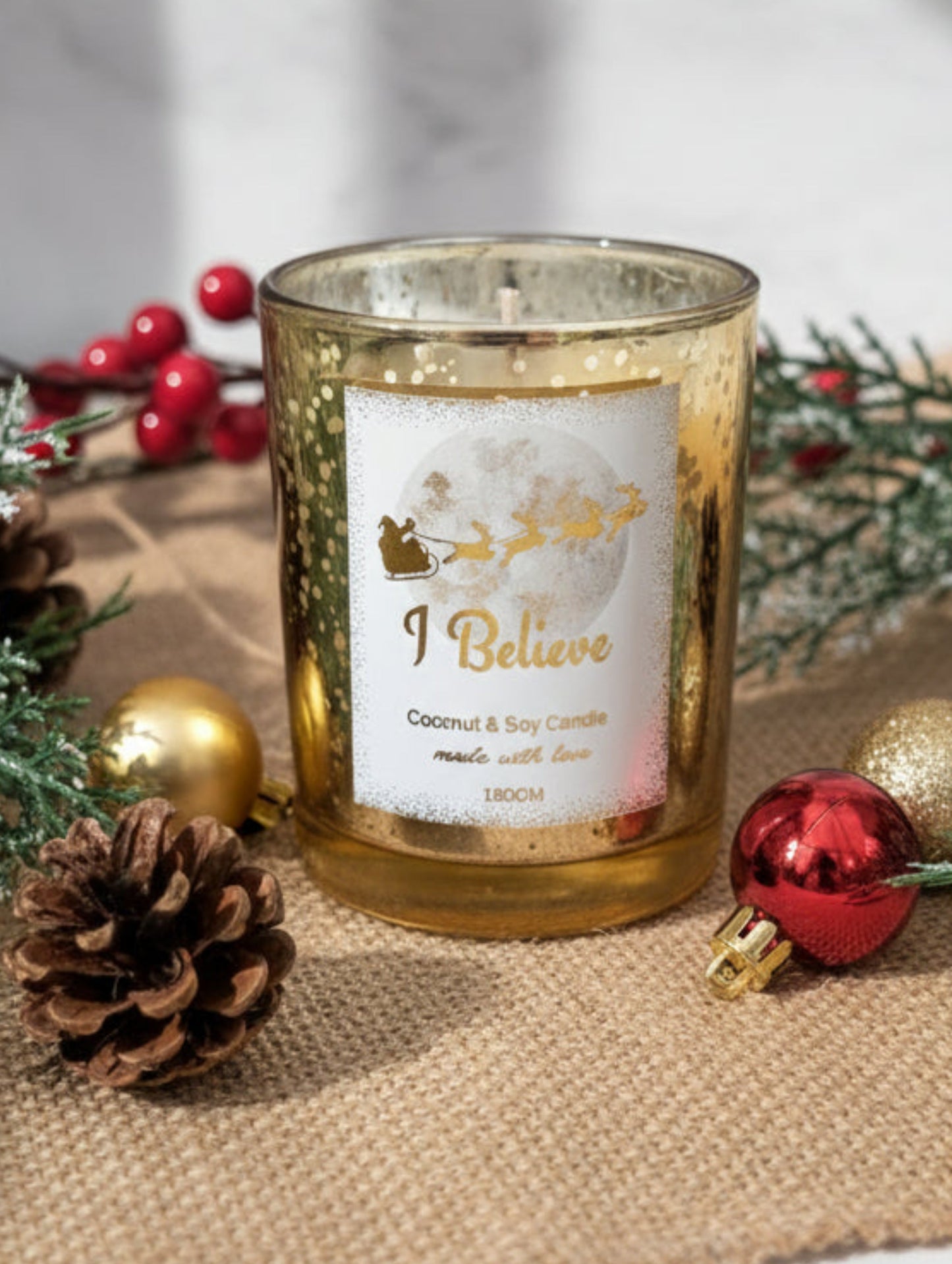 Gold Christmas Decorative candle with 'I Believe' text on a table with Christmas decorations.