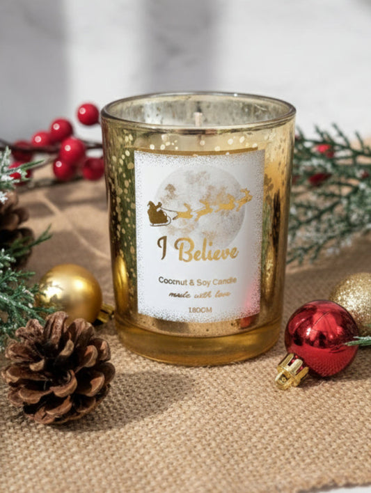 Gold Christmas Decorative candle with 'I Believe' text on a table with Christmas decorations.