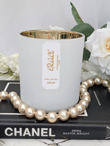 Luxury white candle with gold interior on a Chanel book, surrounded by pearls and white flowers.