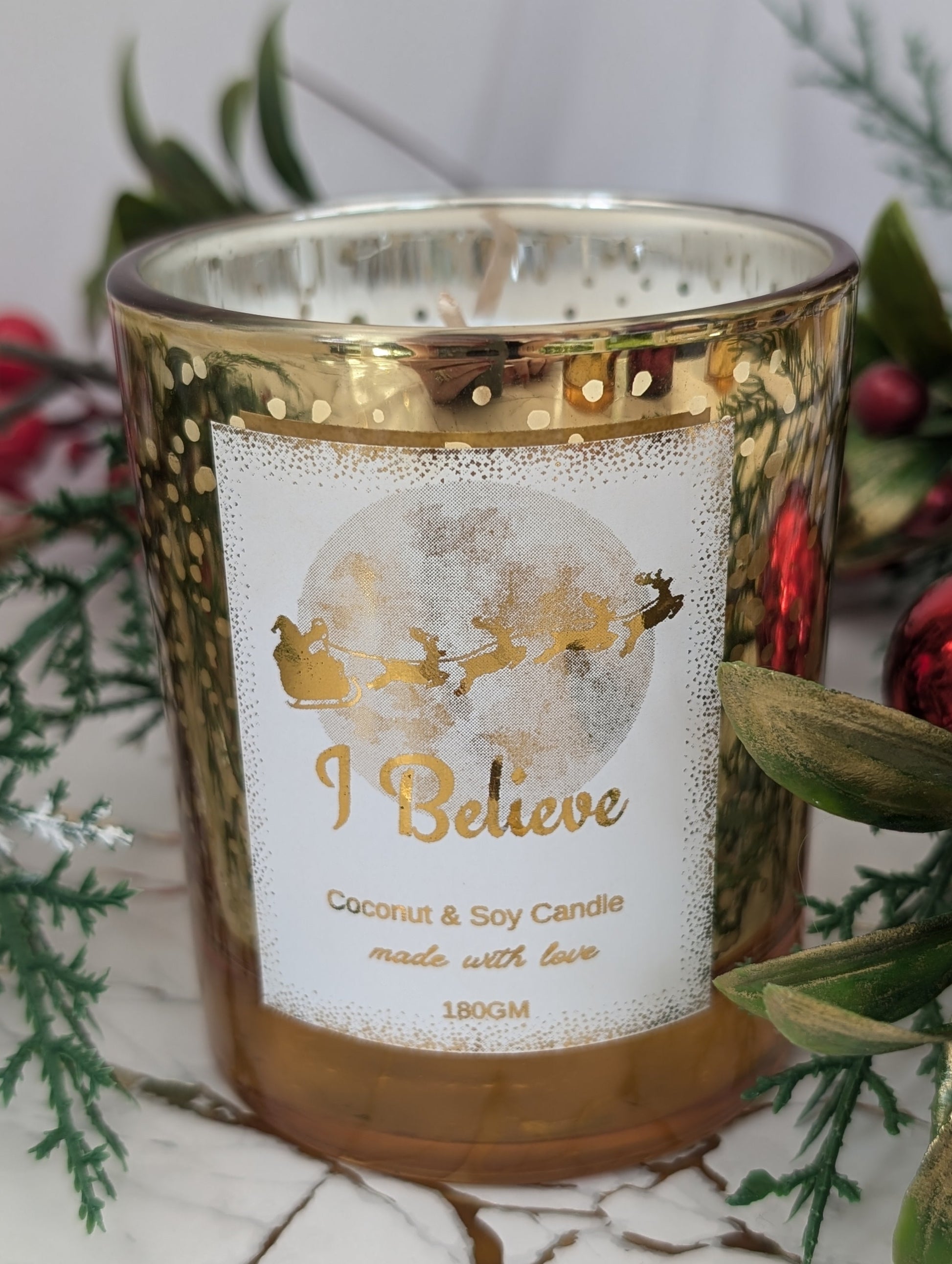 Candle with 'I Believe' label surrounded by festive decorations on a marble surface