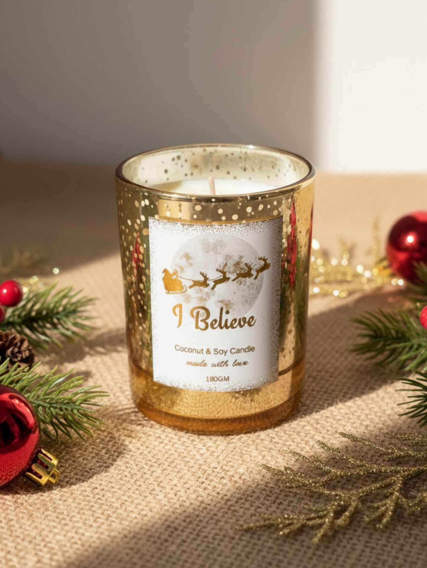 Gold candle with 'I Believe' label surrounded by Christmas decorations on a textured surface