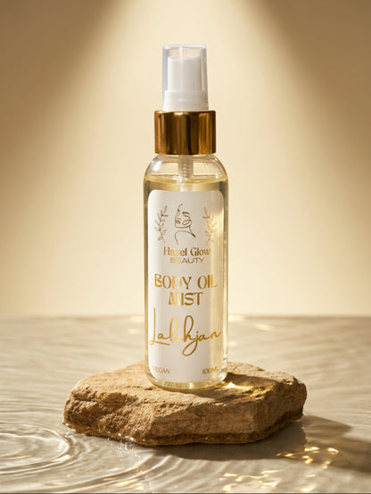 A clear spray bottle of  Lalehjan Body Oil Mist by Hazel Glow with a white label and gold lettering, featuring a gold pump collar and white cap, set against a rough stone plinth in water
