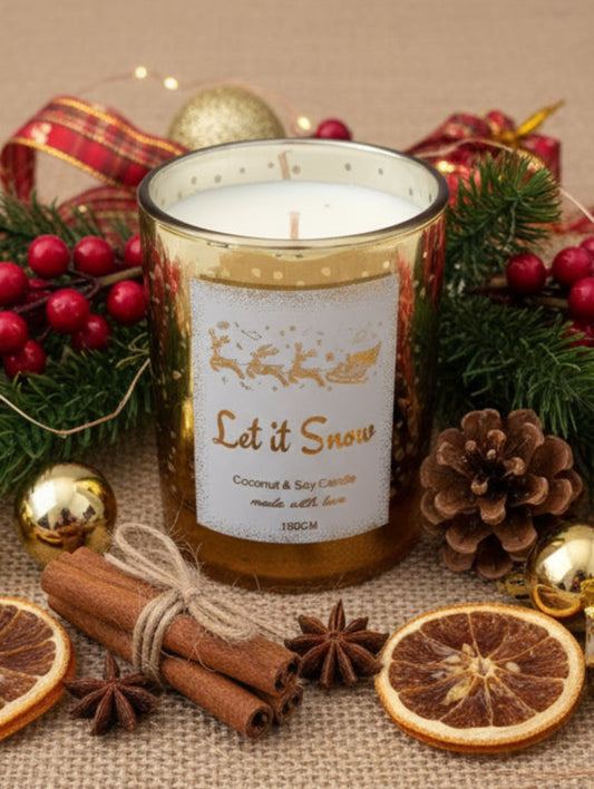 Candle with 'Let it Snow' label and reindeer design, surrounded by greenery on a marble surface.