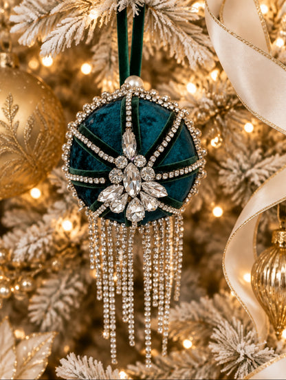 A round teal velvet ornament or decorative hanging piece with silver rhinestone trim, a central crystal flower motif, and dangling silver chain fringe, shown against a frosted Chrstmas tree