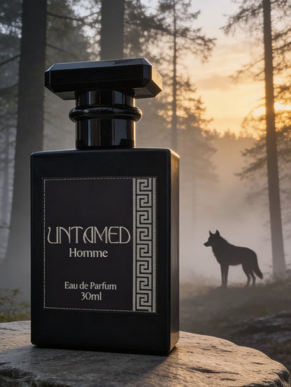 A black rectangular Men's perfume bottle labeled 'UNTAMED Homme' stands on a large stone in a misty forest at sunrise, with a wolf silhouette visible in the background.