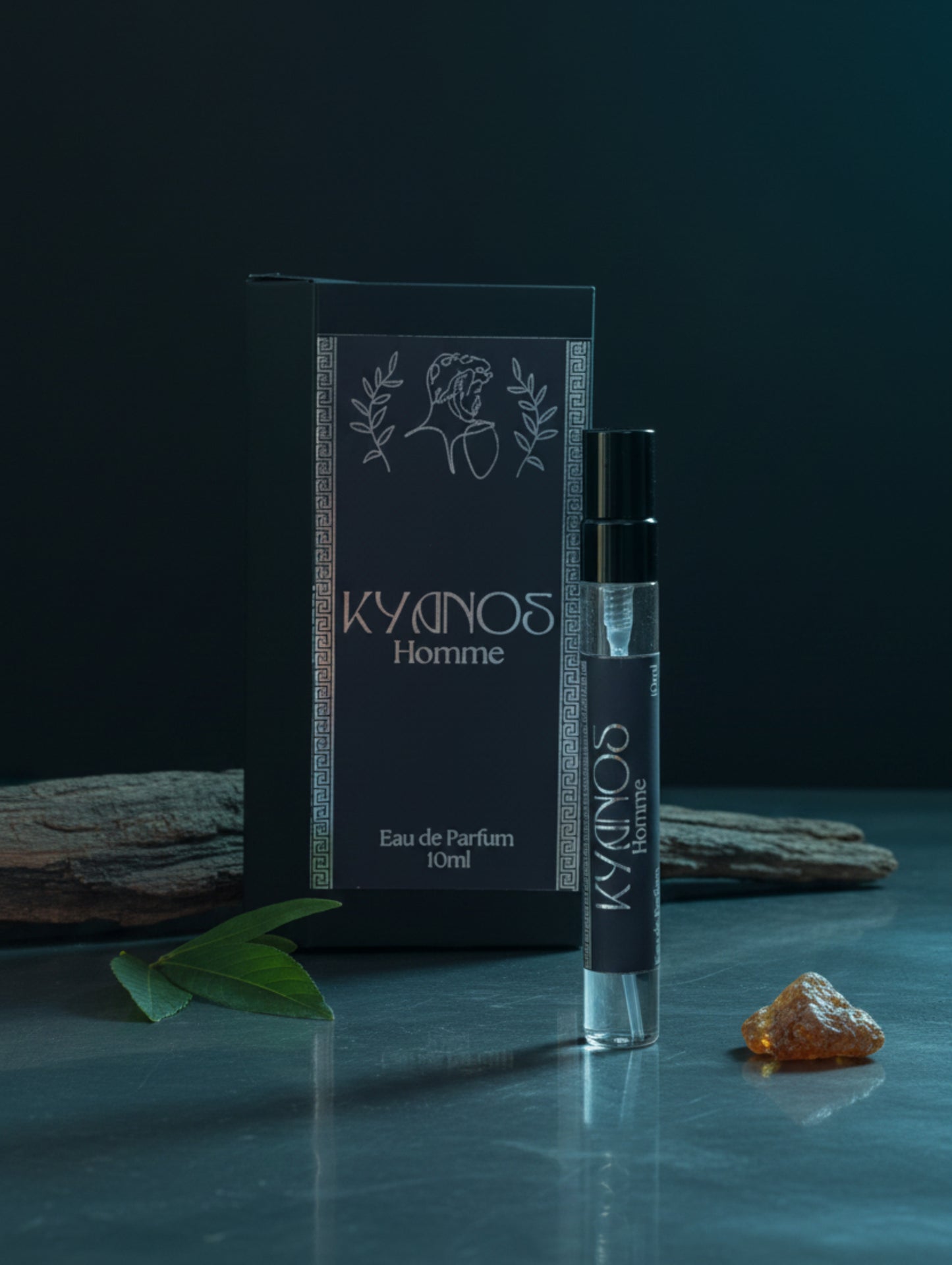 A 10ml perfume atomizer bottle labeled 'KYDINOS Homme' stands in front of its matching black packaging box on a reflective surface against a dark grey background.