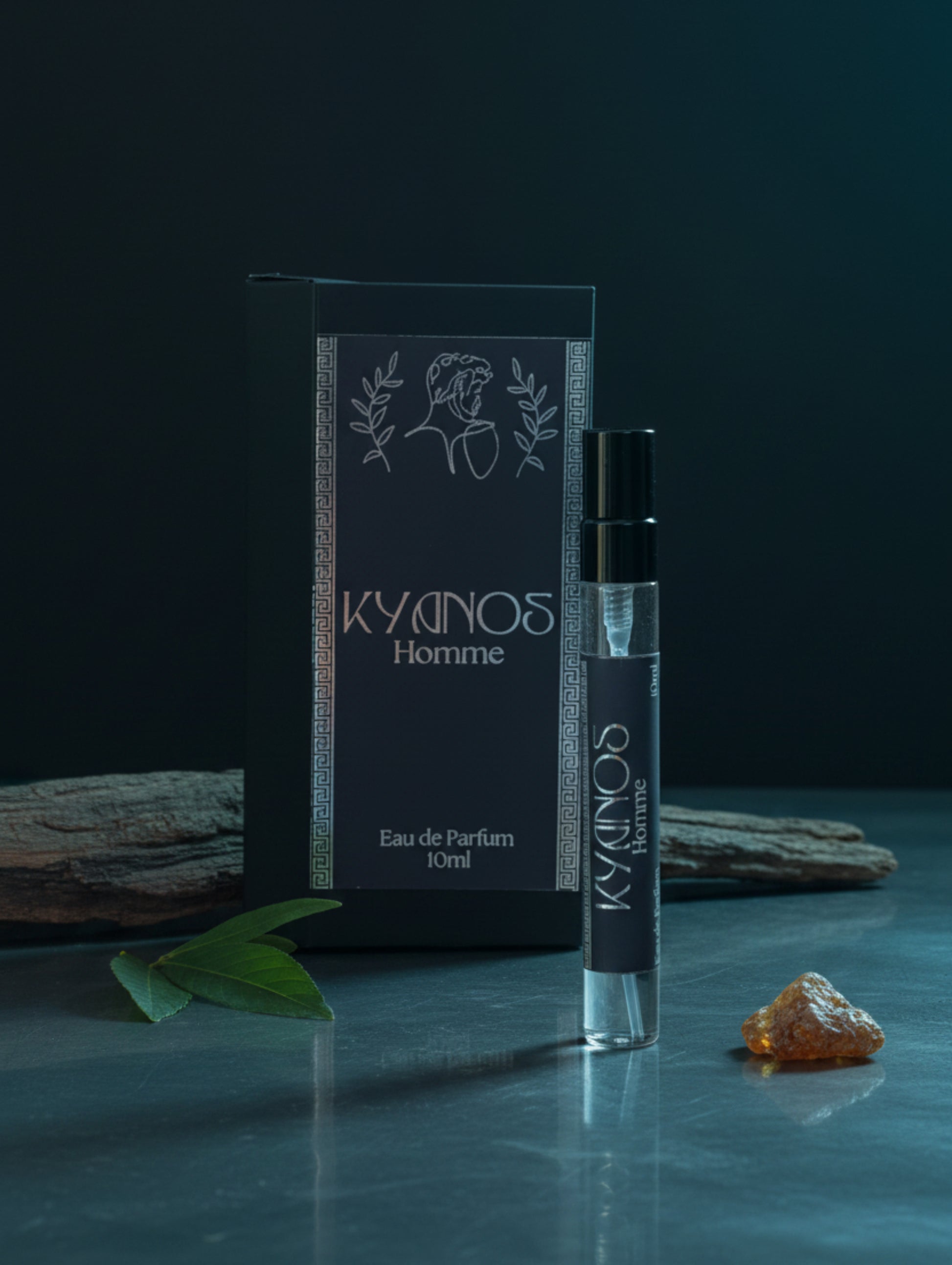 A 10ml perfume atomizer bottle labeled 'KYDINOS Homme' stands in front of its matching black packaging box on a reflective surface against a dark grey background.