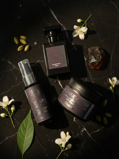 Three Obsidian Homme grooming products arranged on a countertop: a black aftershave balm bottle, a black perfume-style bottle, and a black hair cream jar.