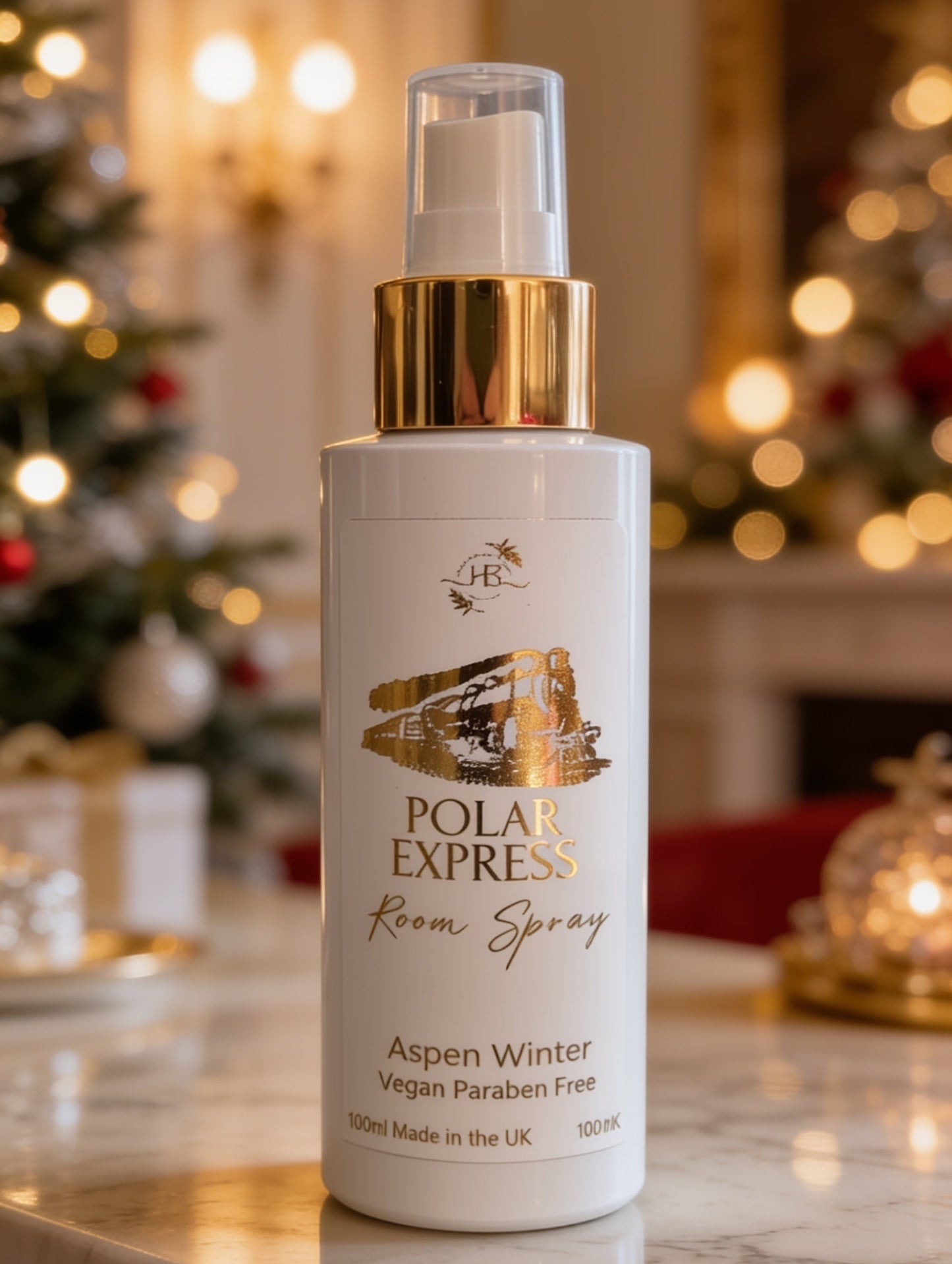A bottle of Polar Express Room Spray with a white body, gold pump collar, and clear cap, set on a marble countertop with a blurred festive holiday background.