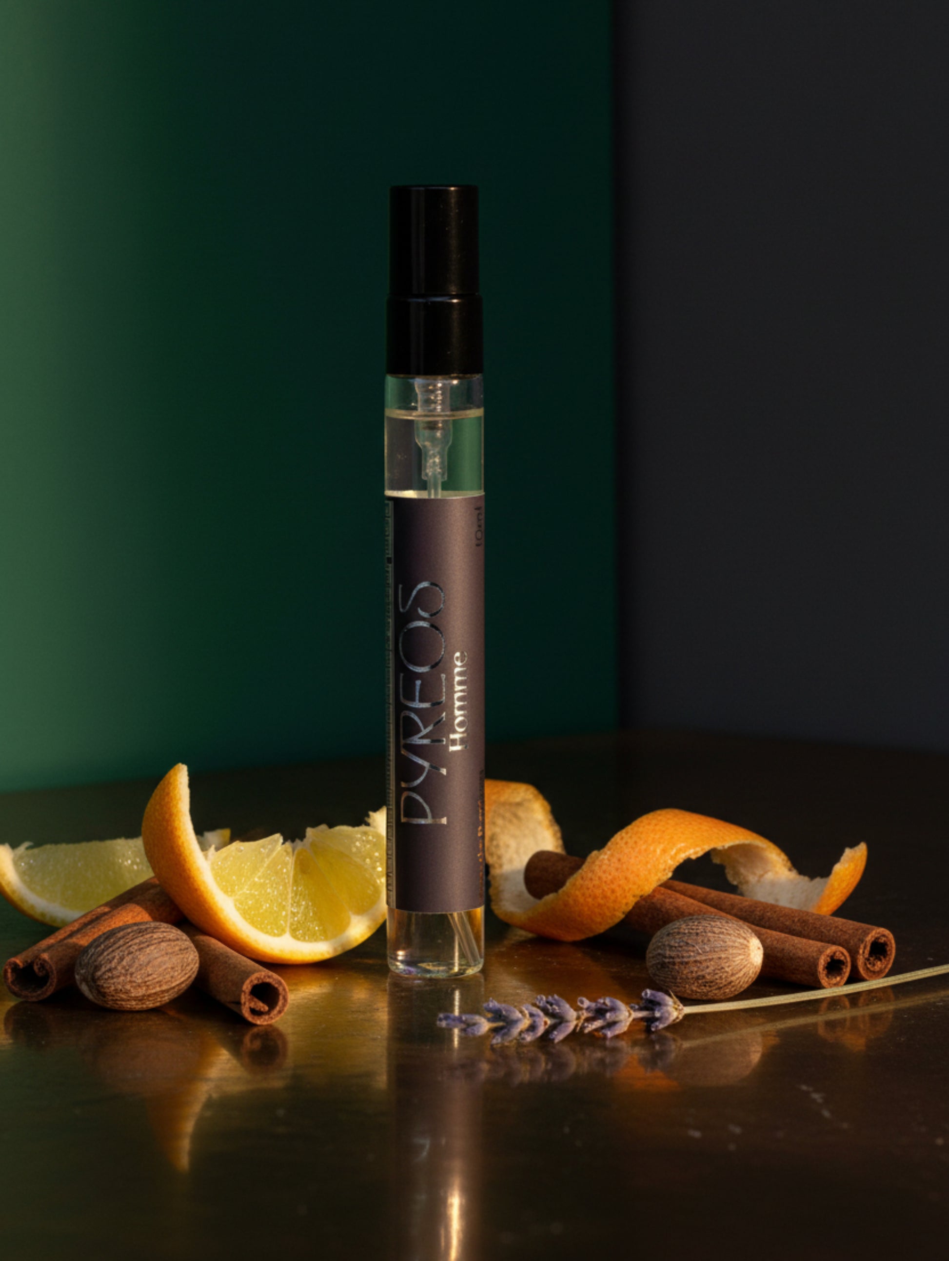 Pyreos Men's Perfume - 10ml travel size, on brown glossy surface with ingredients scattered around it