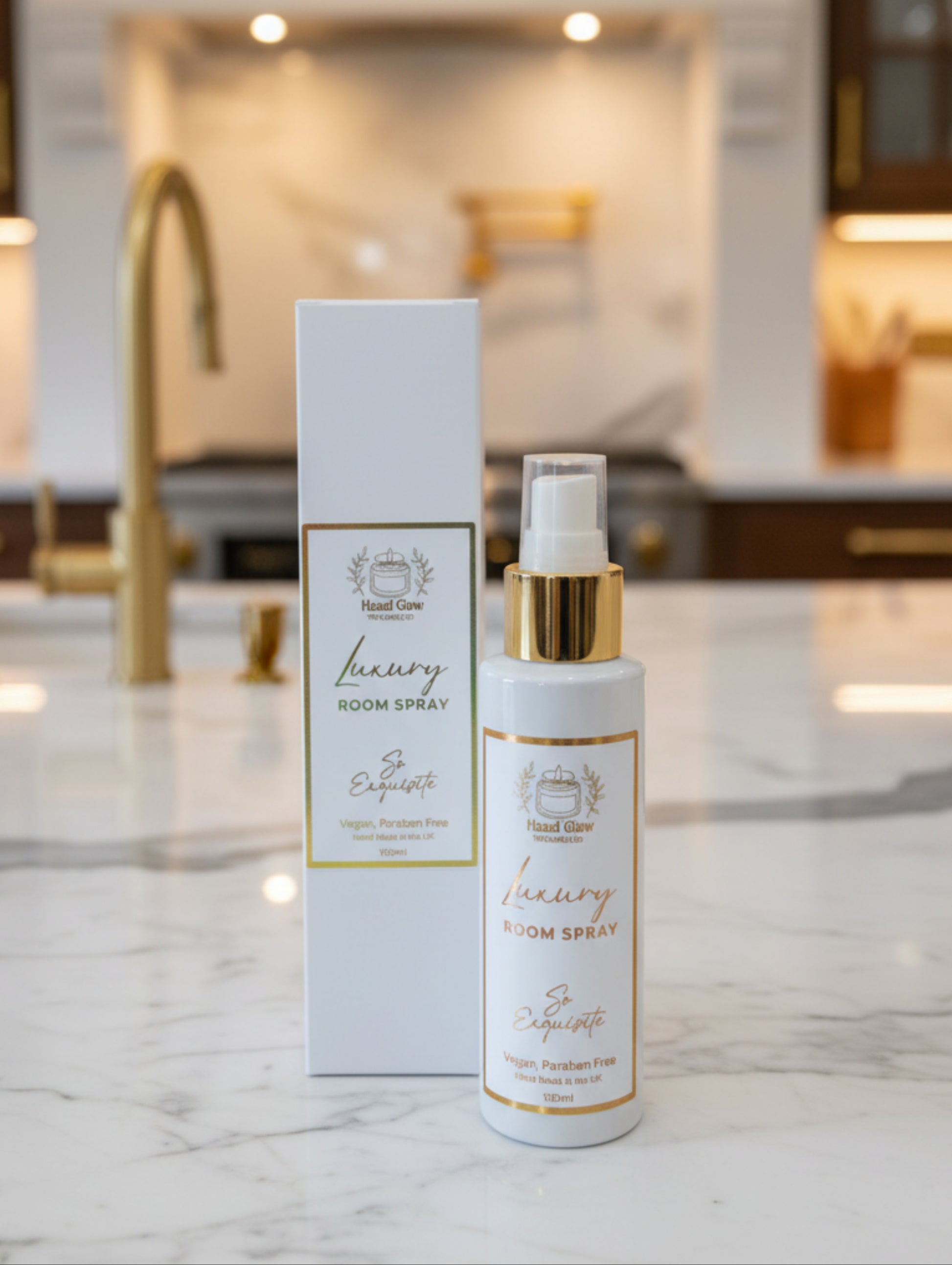 Home fragrance luxury room spray by Hazel Glow.  So Exquisite fragrance - vegan, cruelty free, paraben free.  White bottle with gold cap and white and gold label with white box packaging on a marble counter in a luxury kitchen