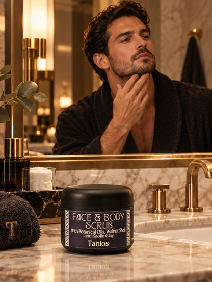 A black jar of Tanios Face & Body Scrub with botanical oils, walnut shell, and kaolin clay, shown in a luxury bathroom with gold taps and a man looking in the mirror