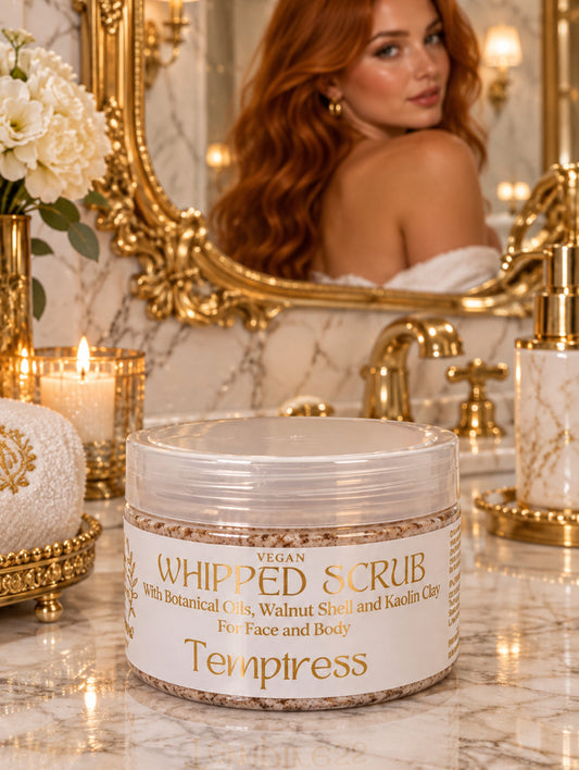 A jar of Temptress Vegan Whipped Scrub with botanical oils, walnut shell, and kaolin clay, shown in a luxury bathroom with ornate mirror