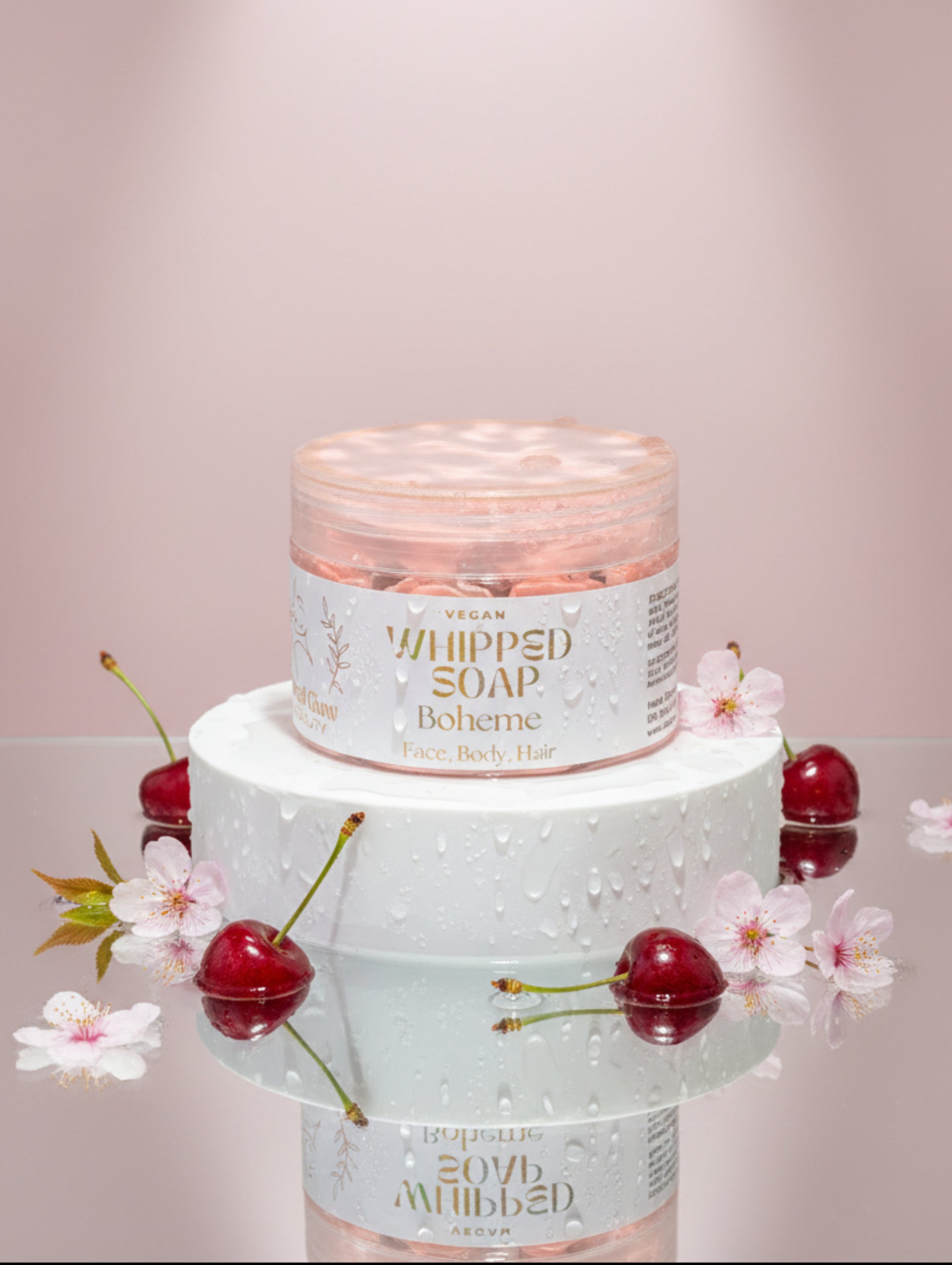 Vegan whipped soap Boheme by Hazel Glow.  jar on white plinth surrounded by cherries and cherry blossom