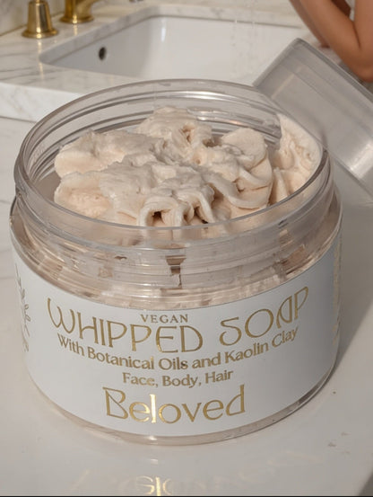 Woman applying whipped soap from a jar labeled 'Beloved' on a bathroom counter.